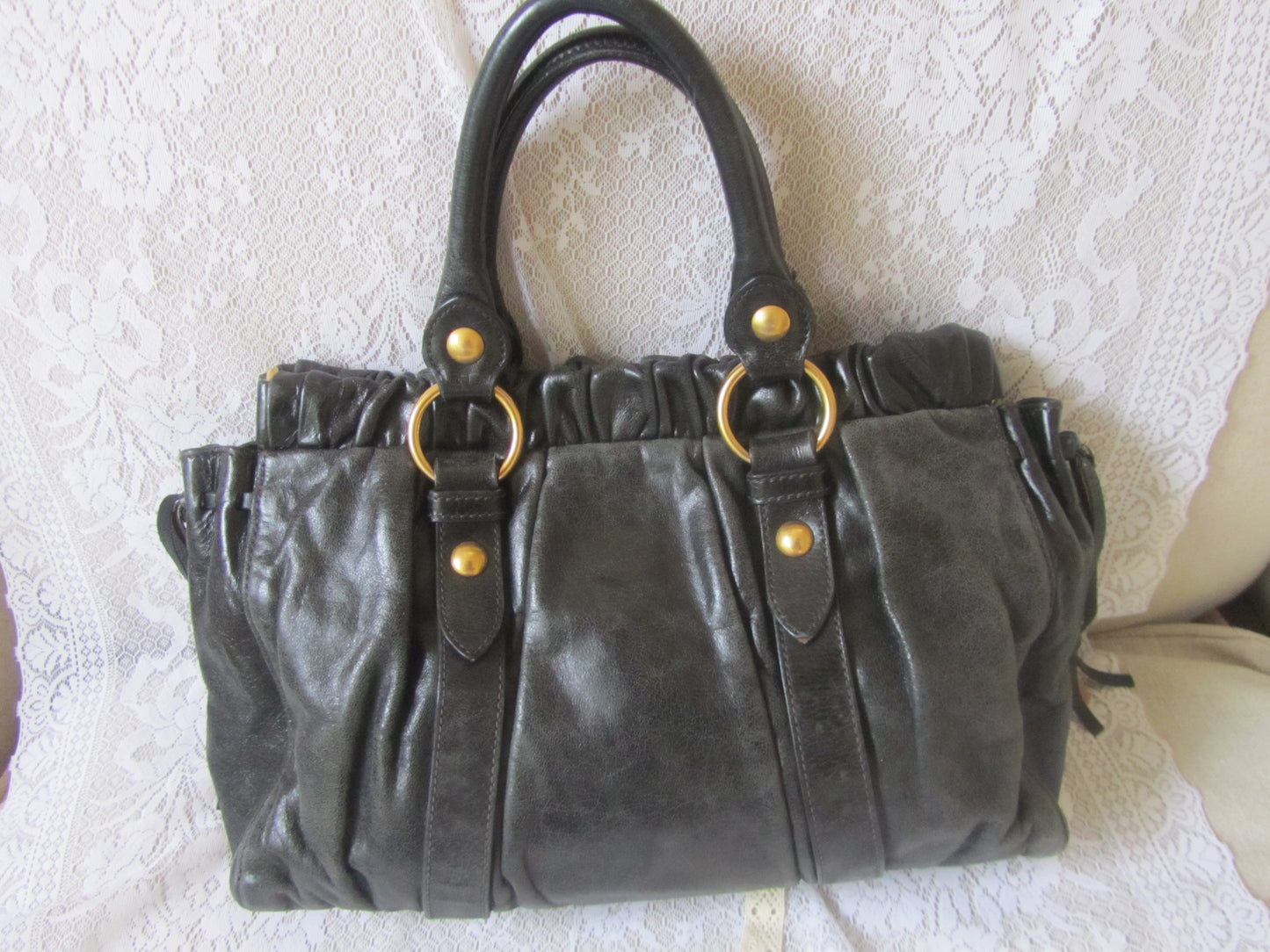 Black leather handbag with gold accents on a textured white surface