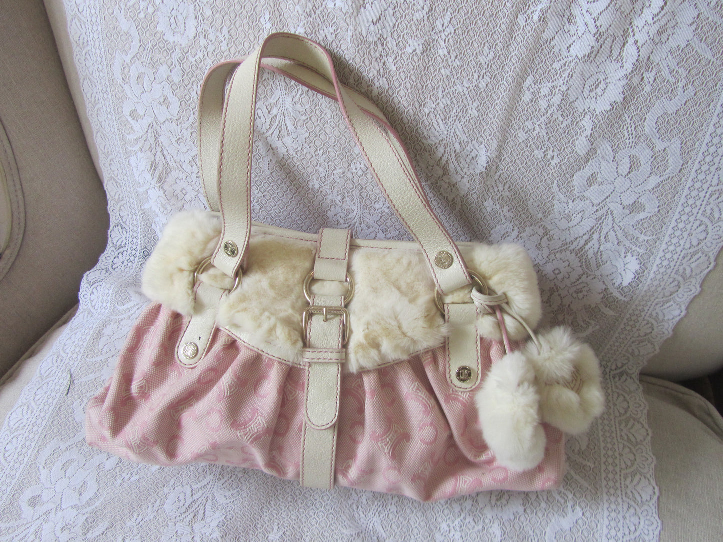 Pink handbag with white fur trim and pom-poms on a lace background