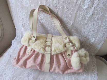Pink handbag with white fur trim and pom-poms on a lace background