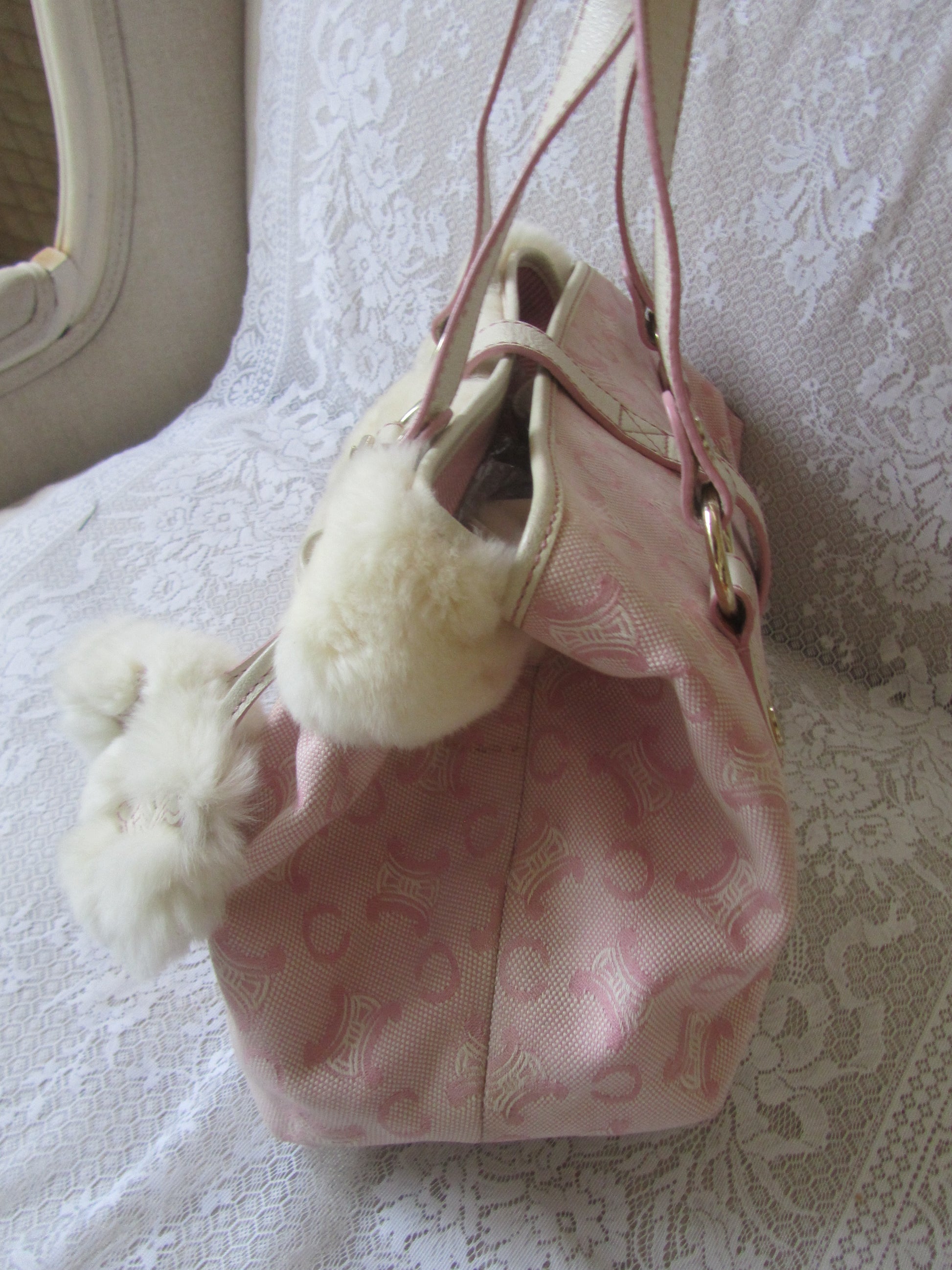 Pink drawstring bag with white pom-poms on a textured surface