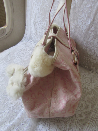 Pink drawstring bag with white pom-poms on a textured surface
