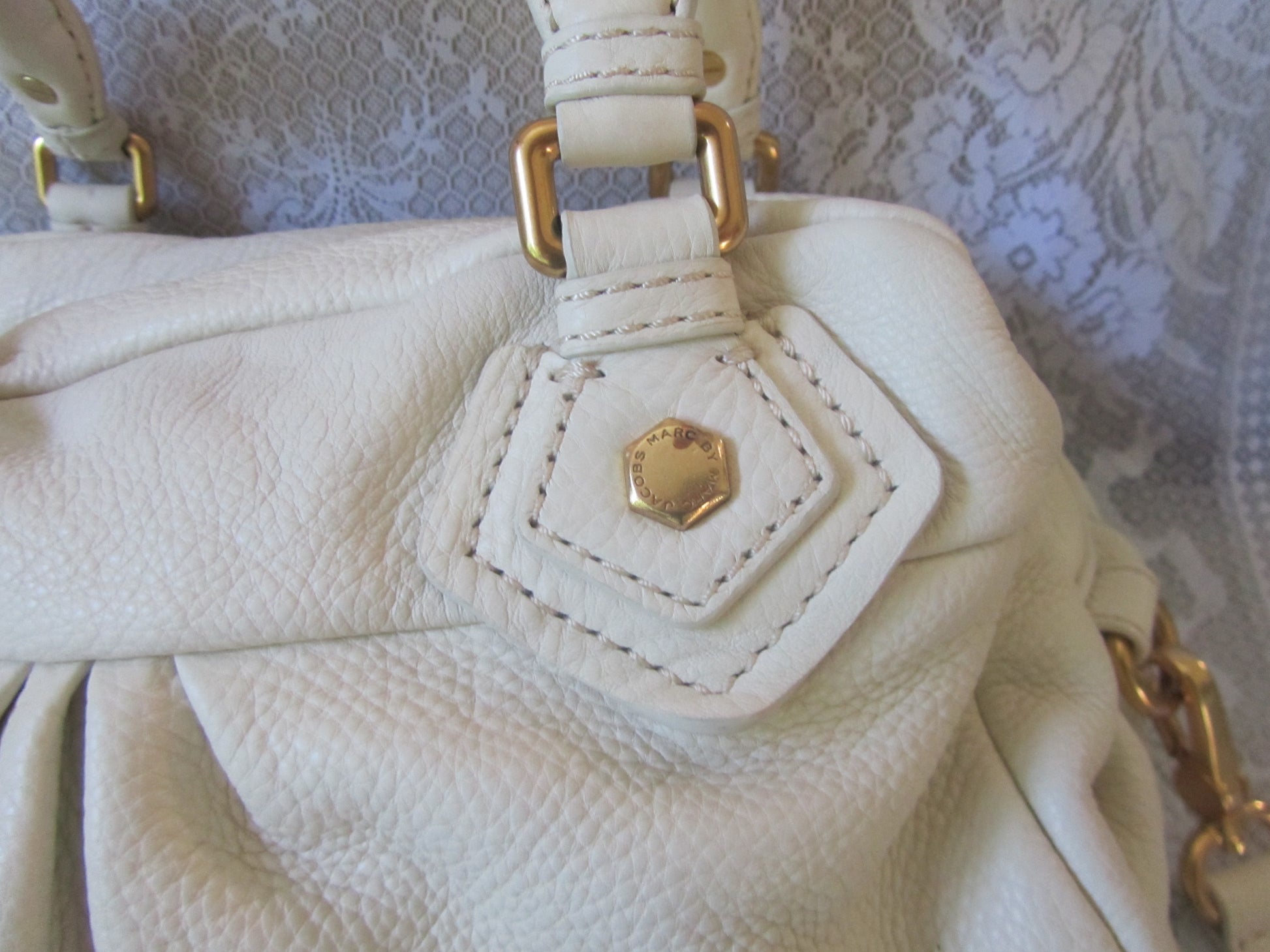 Close-up of a white handbag with gold hardware on a textured background