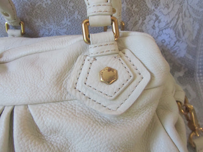 Close-up of a white handbag with gold hardware on a textured background