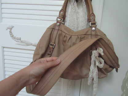 Beige handbag with a strap held by a hand against a white background