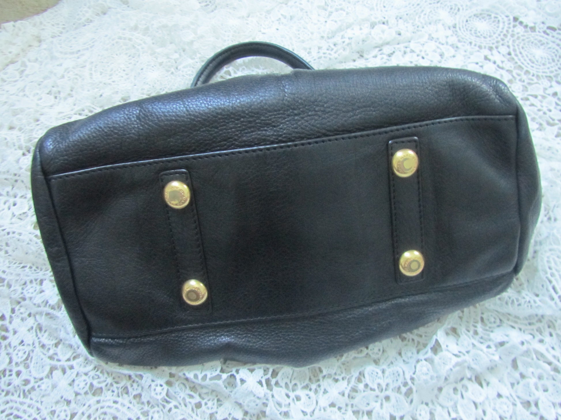 Black leather bag with gold studs on a textured white surface