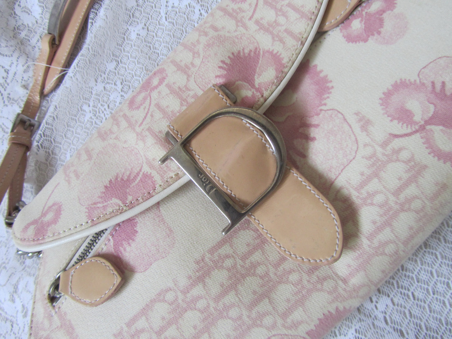 Floral-patterned handbag with a beige strap and silver buckle on a textured white background