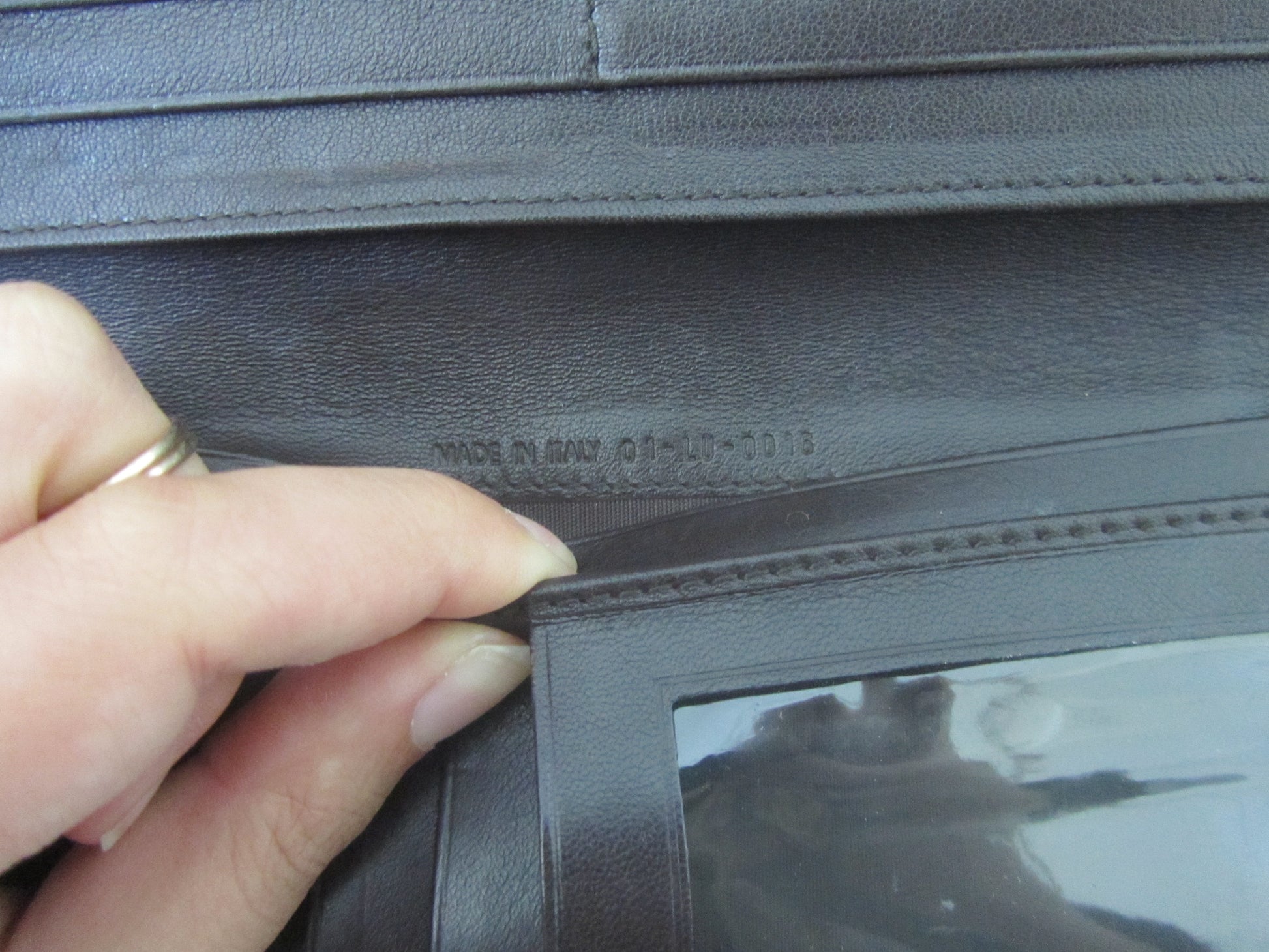 Close-up of a hand holding a dark leather wallet with visible branding.