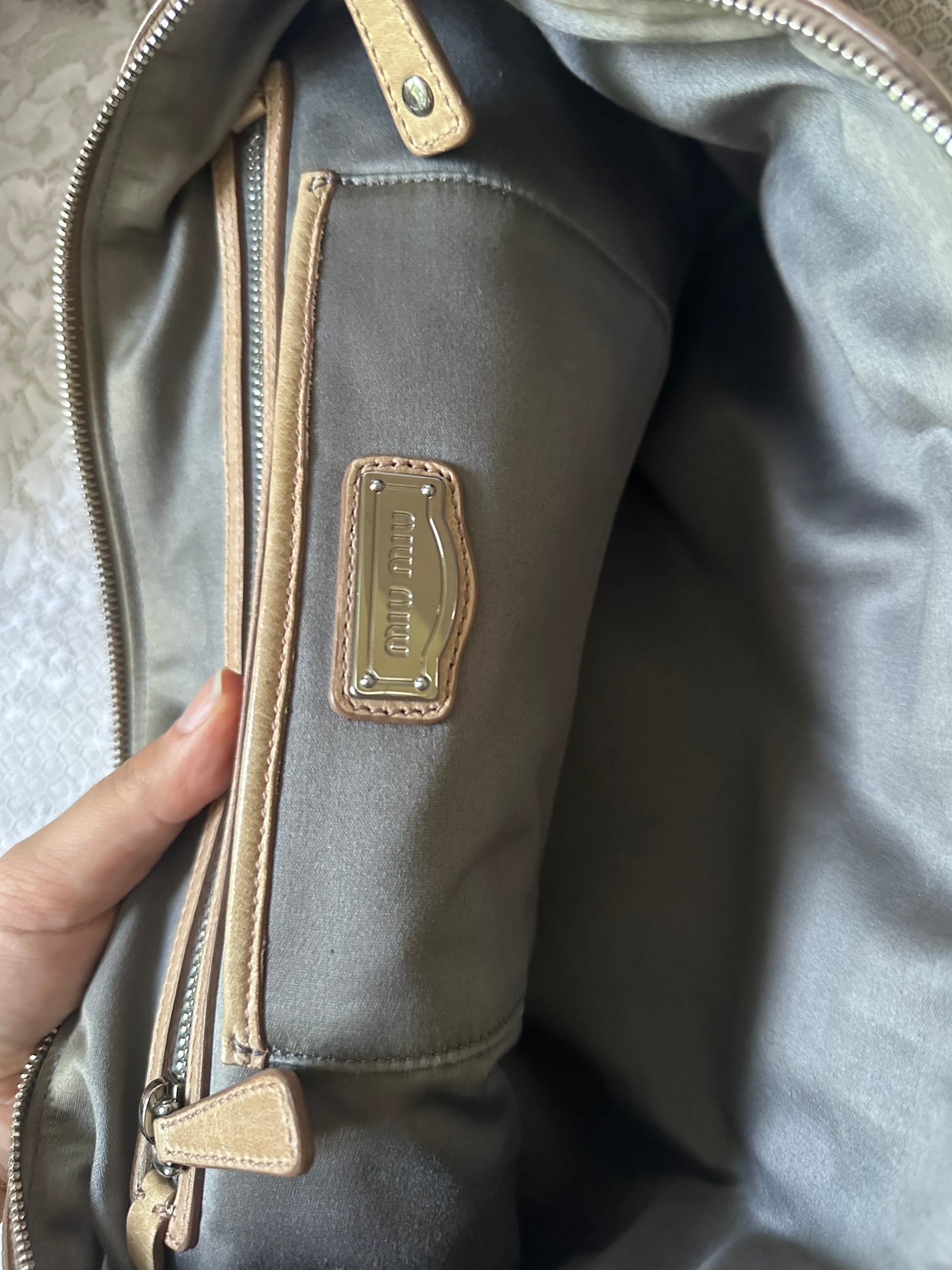 Gray bag with gold zipper and brand logo held by a hand