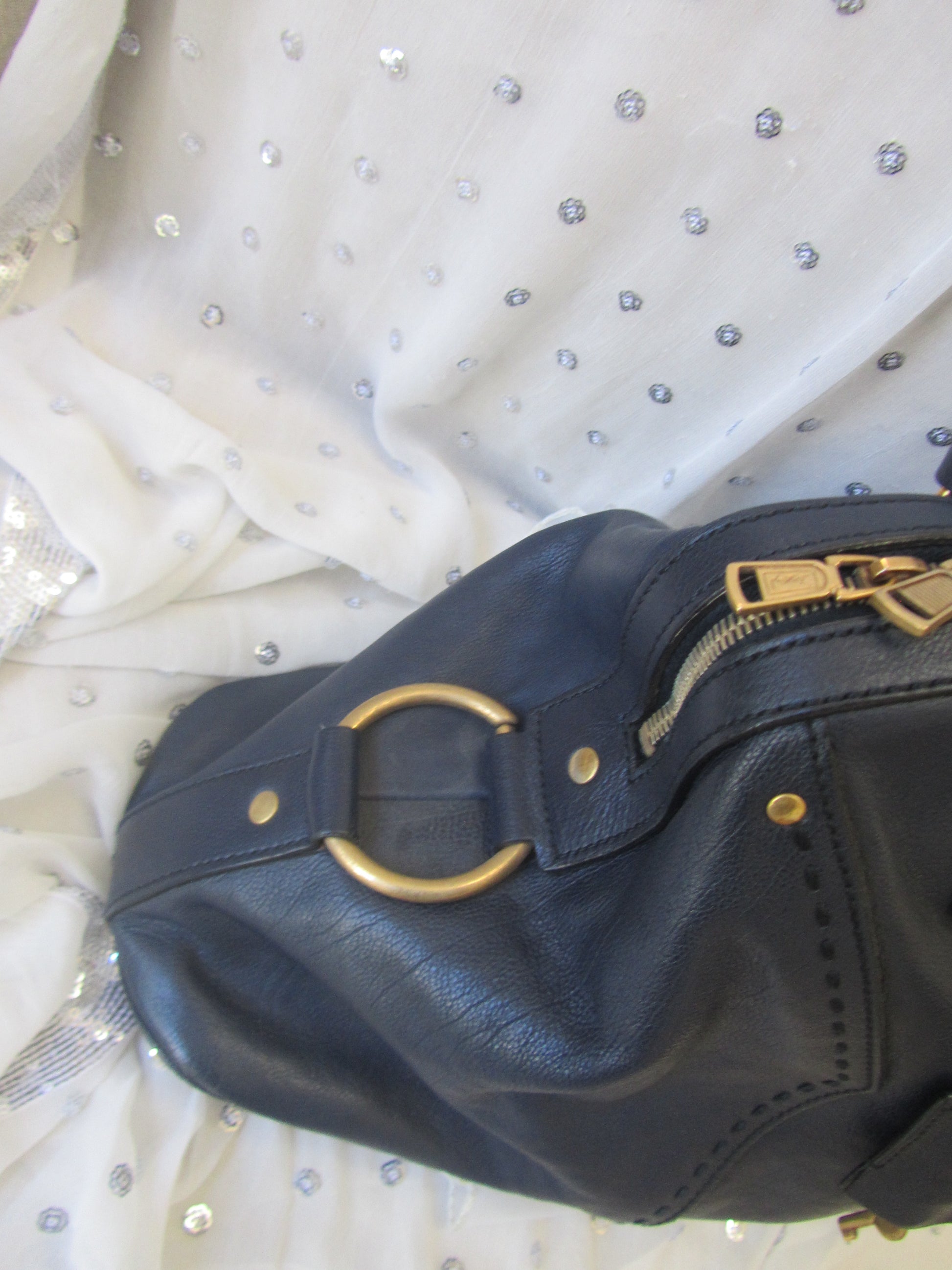 Blue leather handbag with gold accents on a white fabric background