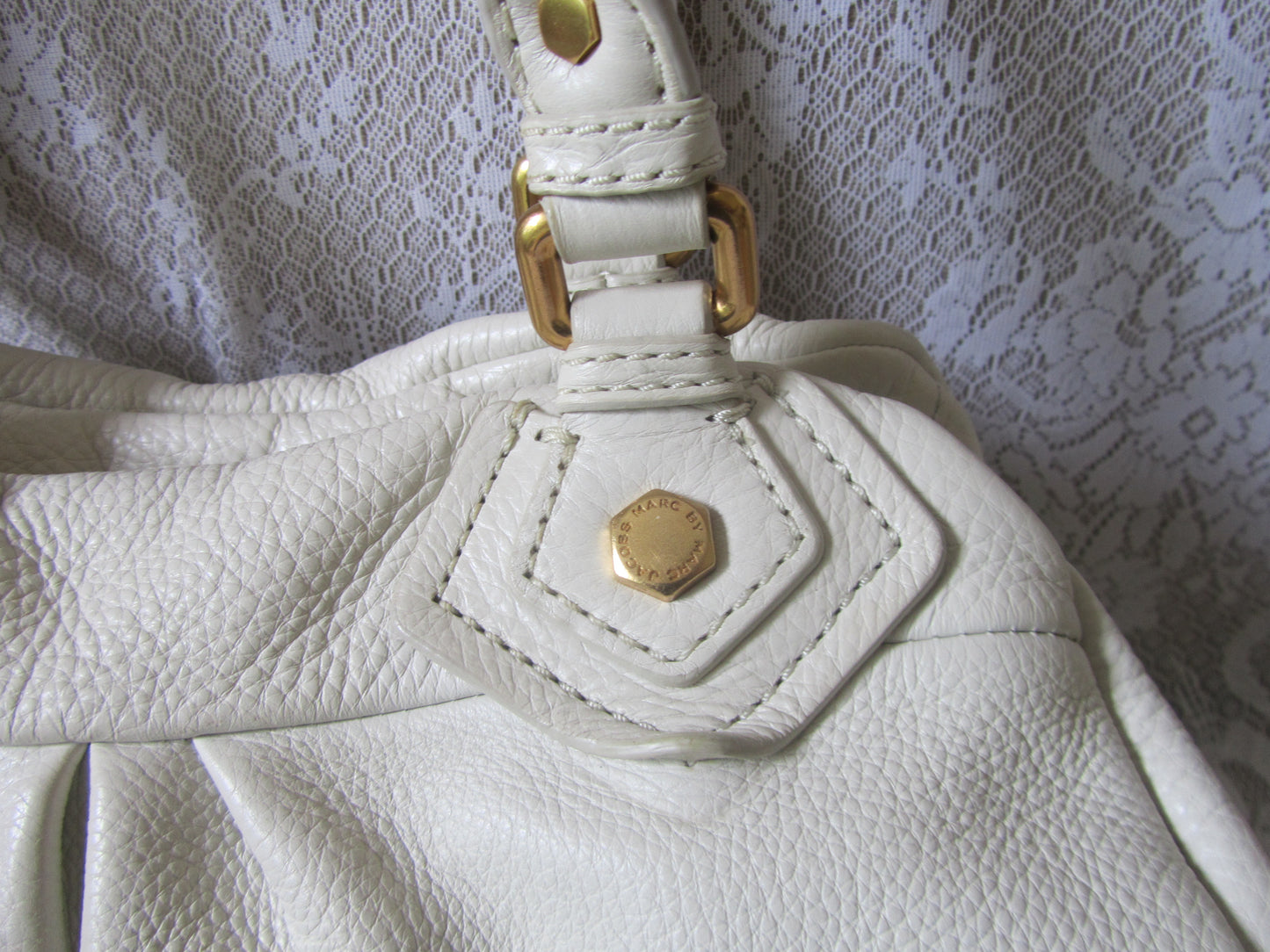 Close-up of a white leather handbag with gold hardware on a textured white background