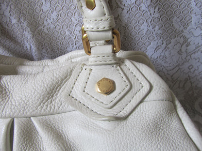 Close-up of a white leather handbag with gold hardware on a textured white background