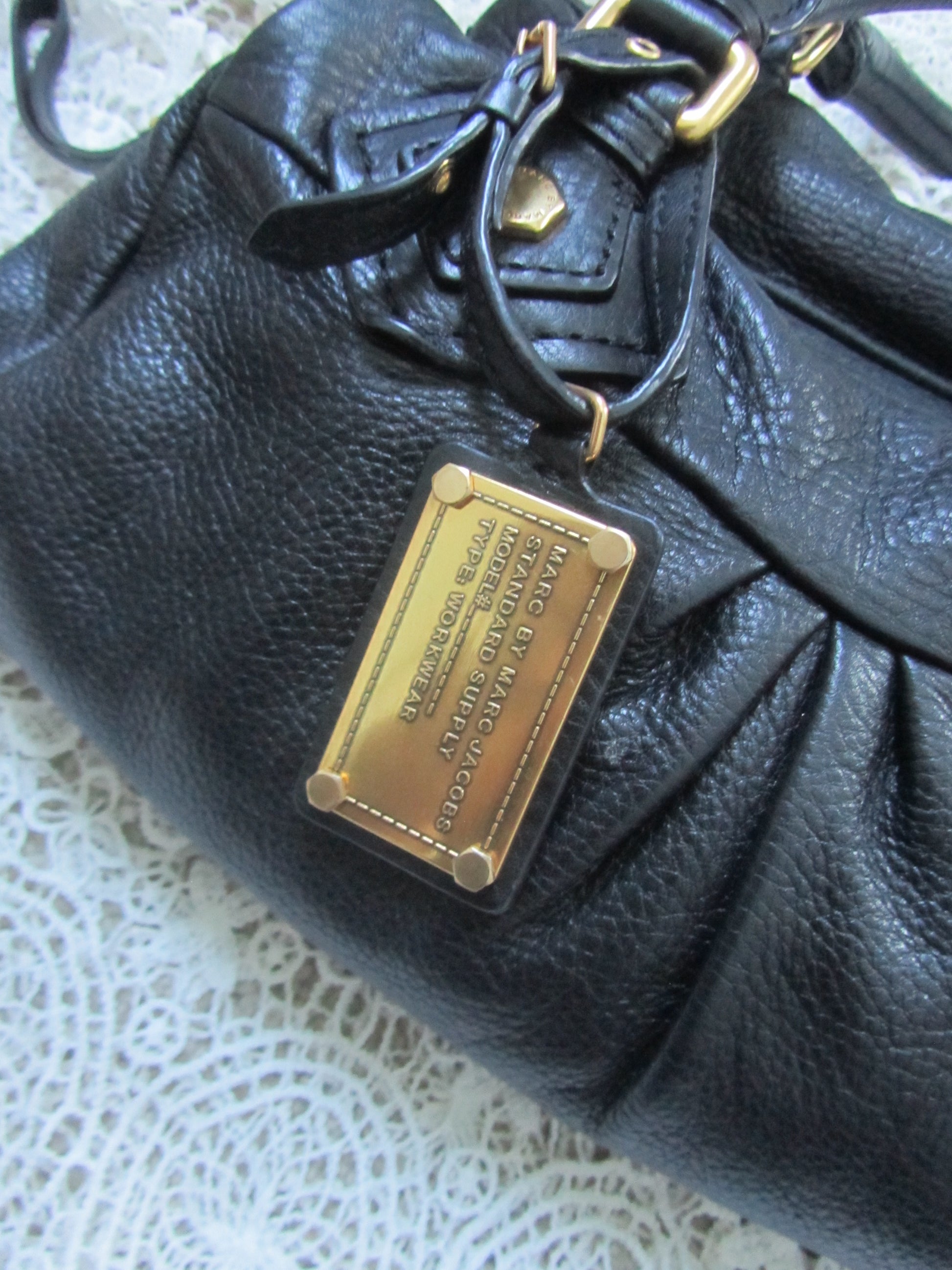 Black leather handbag with a gold Marc by Marc Jacobs tag on a textured surface.