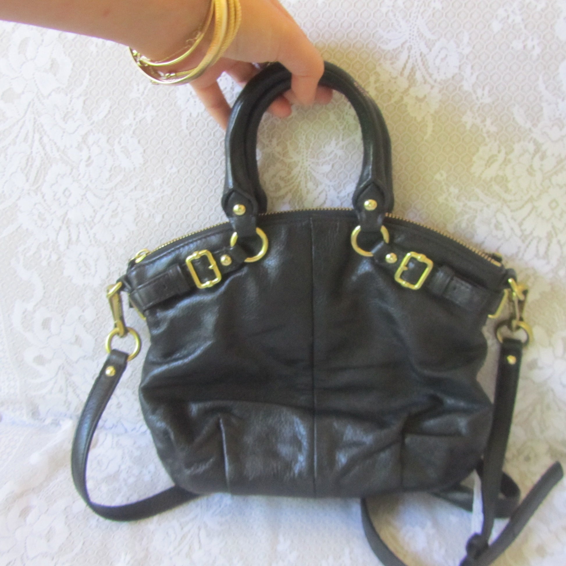 Black handbag with gold hardware held by a hand on a textured white surface