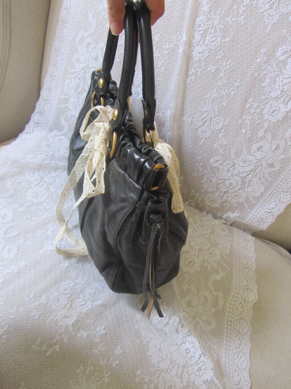 Black leather bag with lace details held over a white textured surface