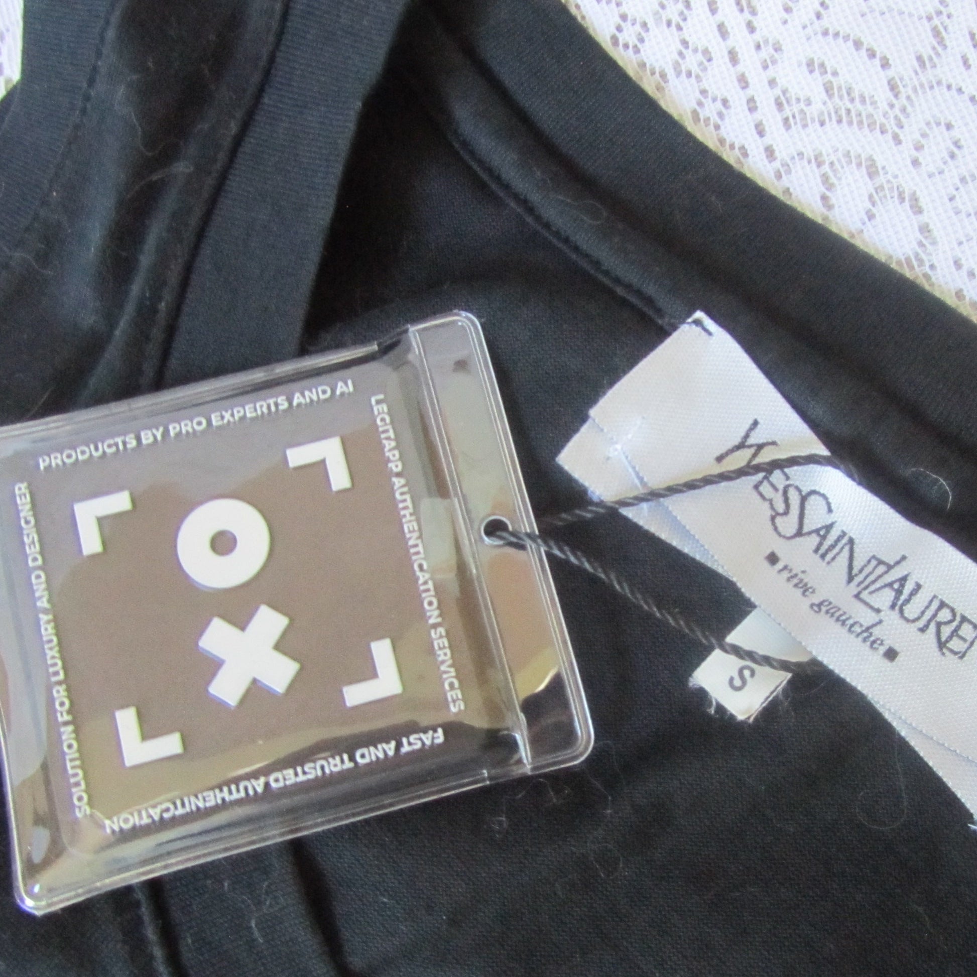 Close-up of a Yves Saint Laurent tag on a black garment with a clear plastic card.