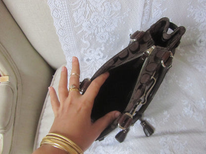 Hand reaching into a brown leather handbag with gold accents on a textured white surface.
