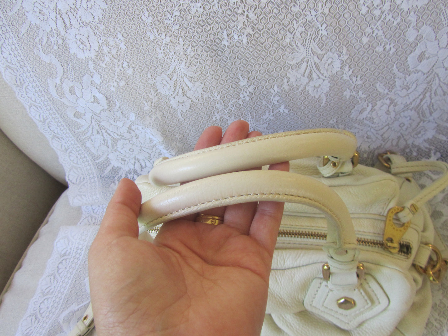 Hand holding a cream-colored handbag with gold accents against a textured white background