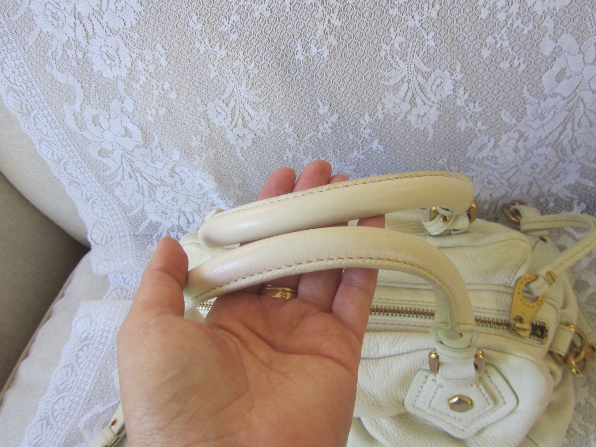 Hand holding a cream-colored handbag with gold accents against a textured white background