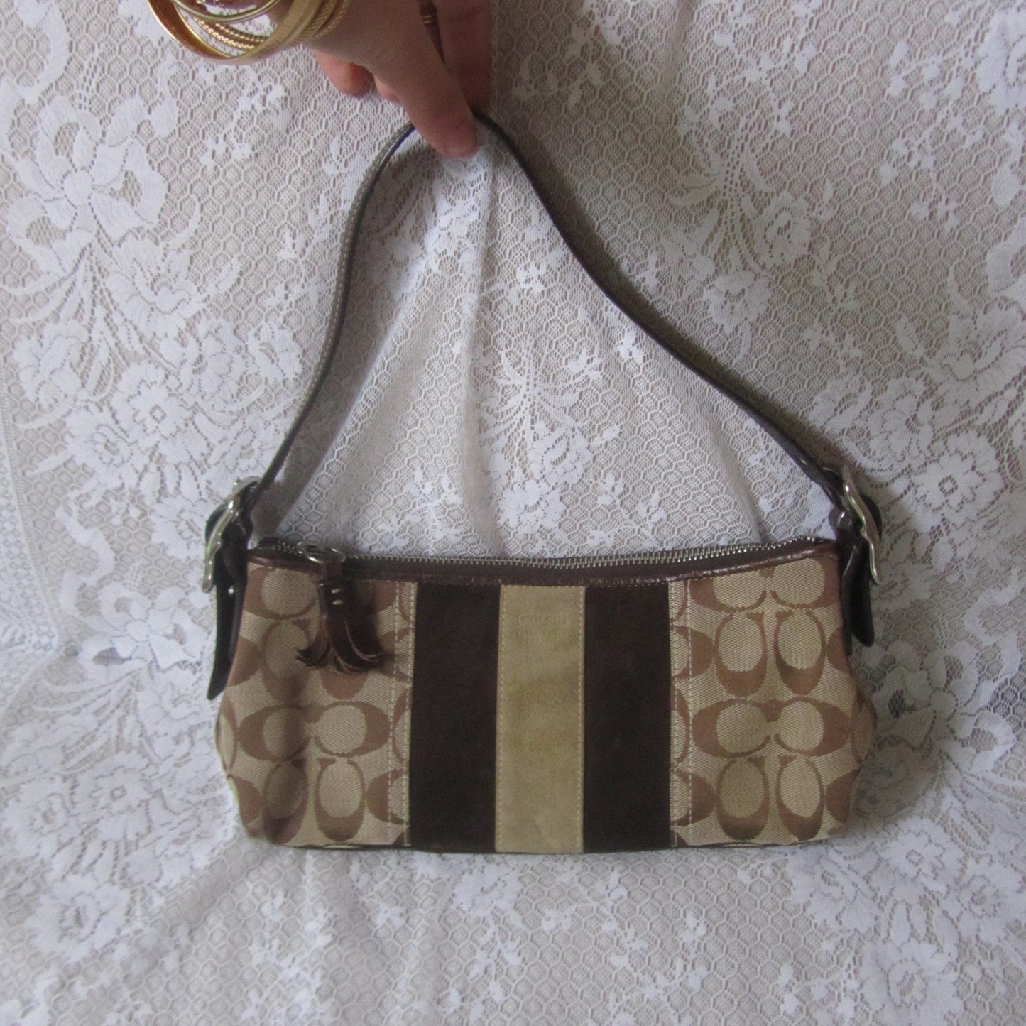 Patterned handbag on a textured surface with a hand holding the strap.