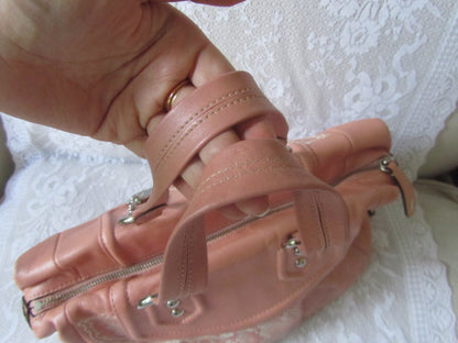 Close-up of a pink leather handbag with zippers on a white lace background