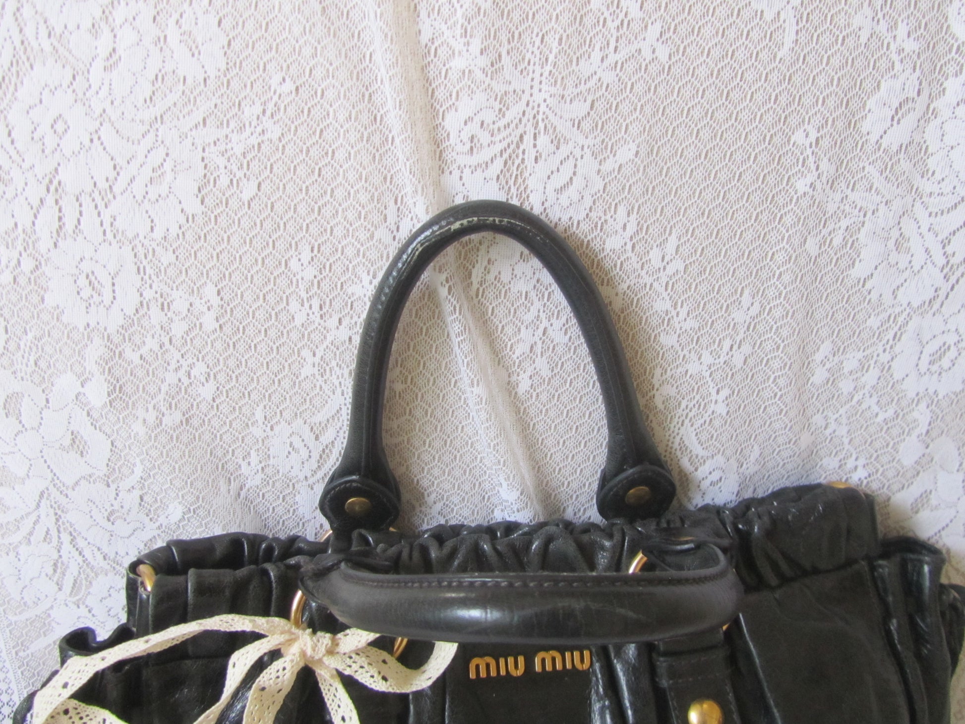 Black handbag with 'Miu Miu' logo on a textured white background