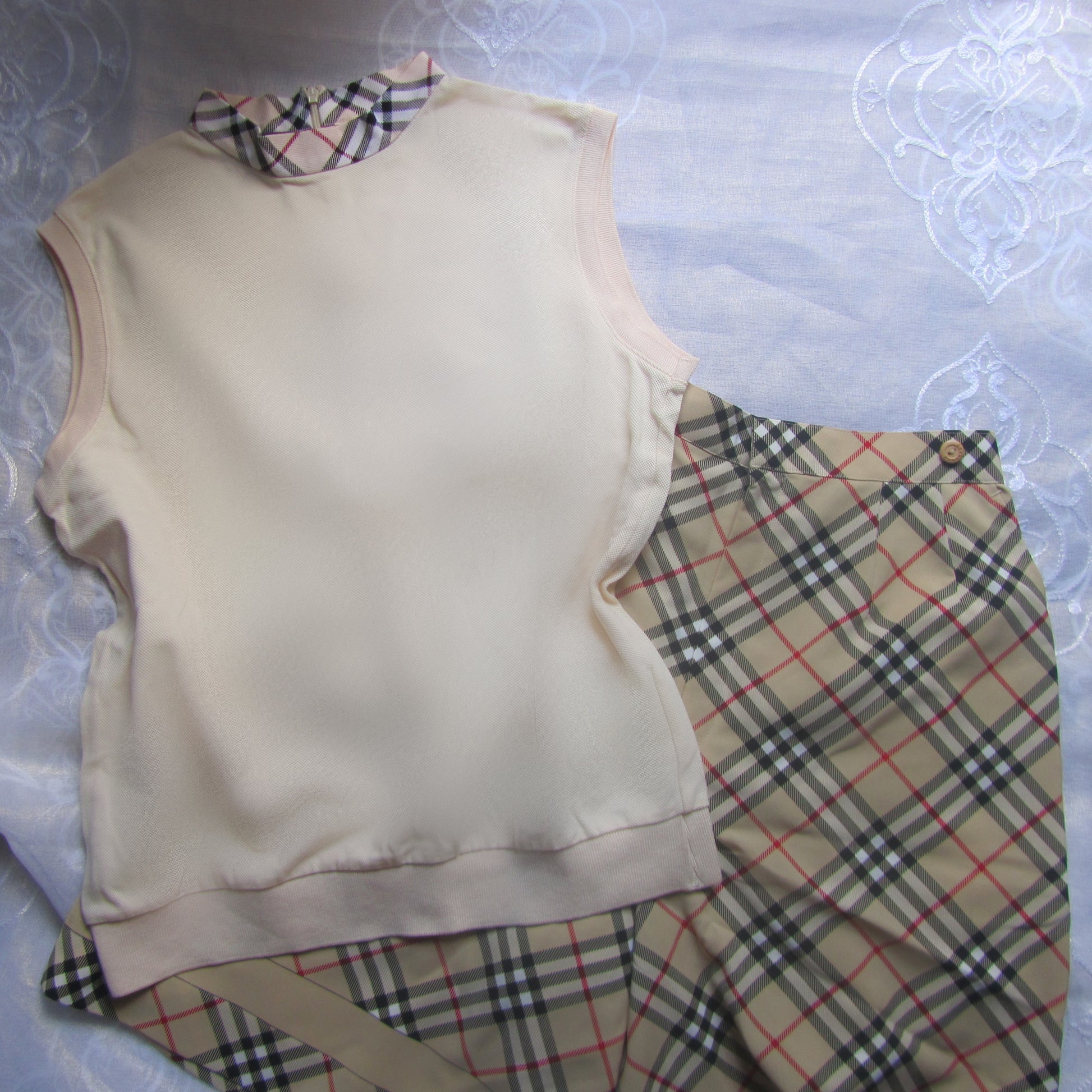 Beige sleeveless top and plaid shorts on a textured surface