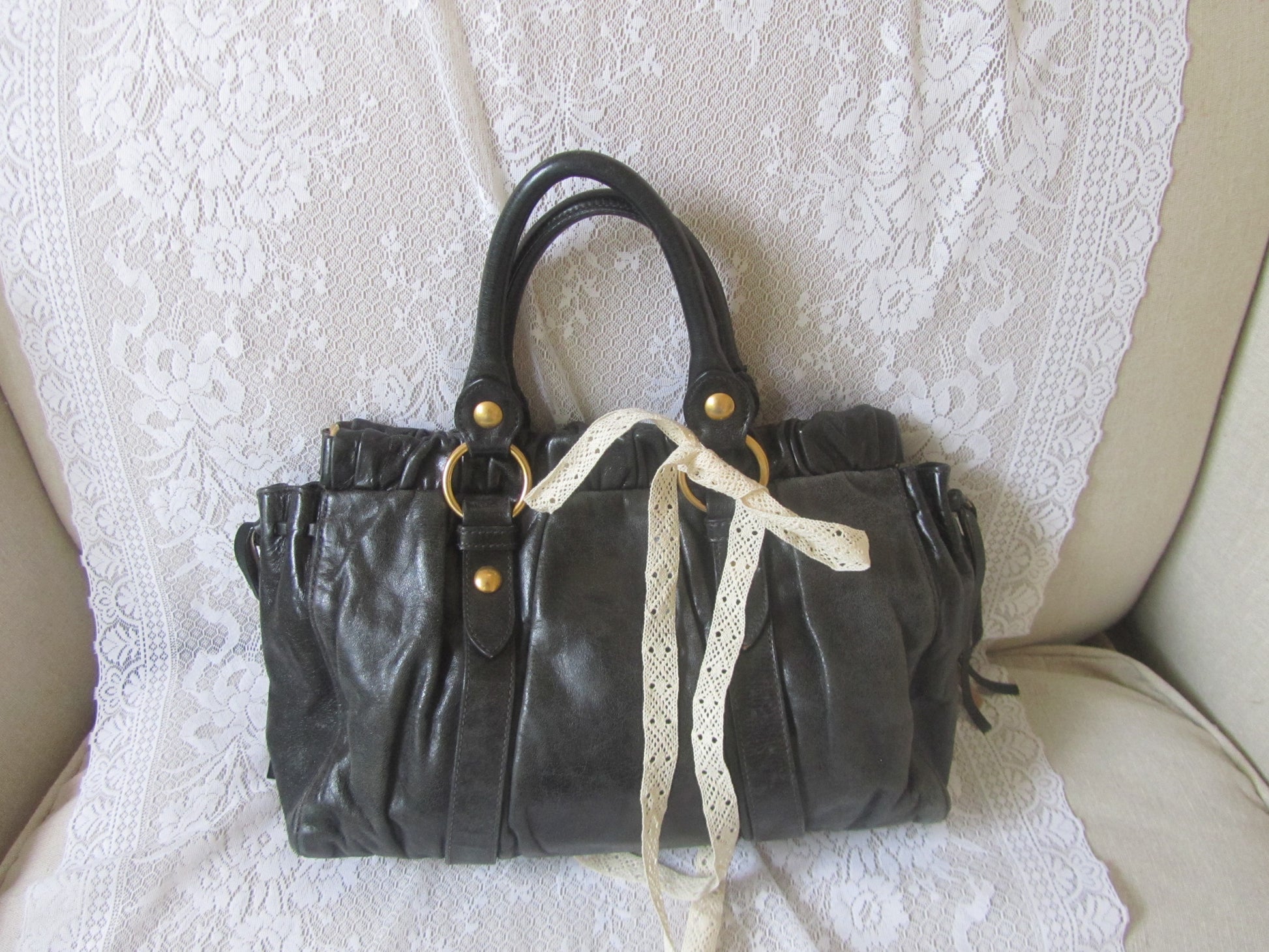 Black leather handbag with gold accents on a white lace fabric background