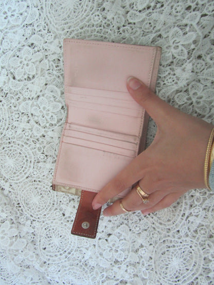 Hand holding a pink wallet on a textured white surface
