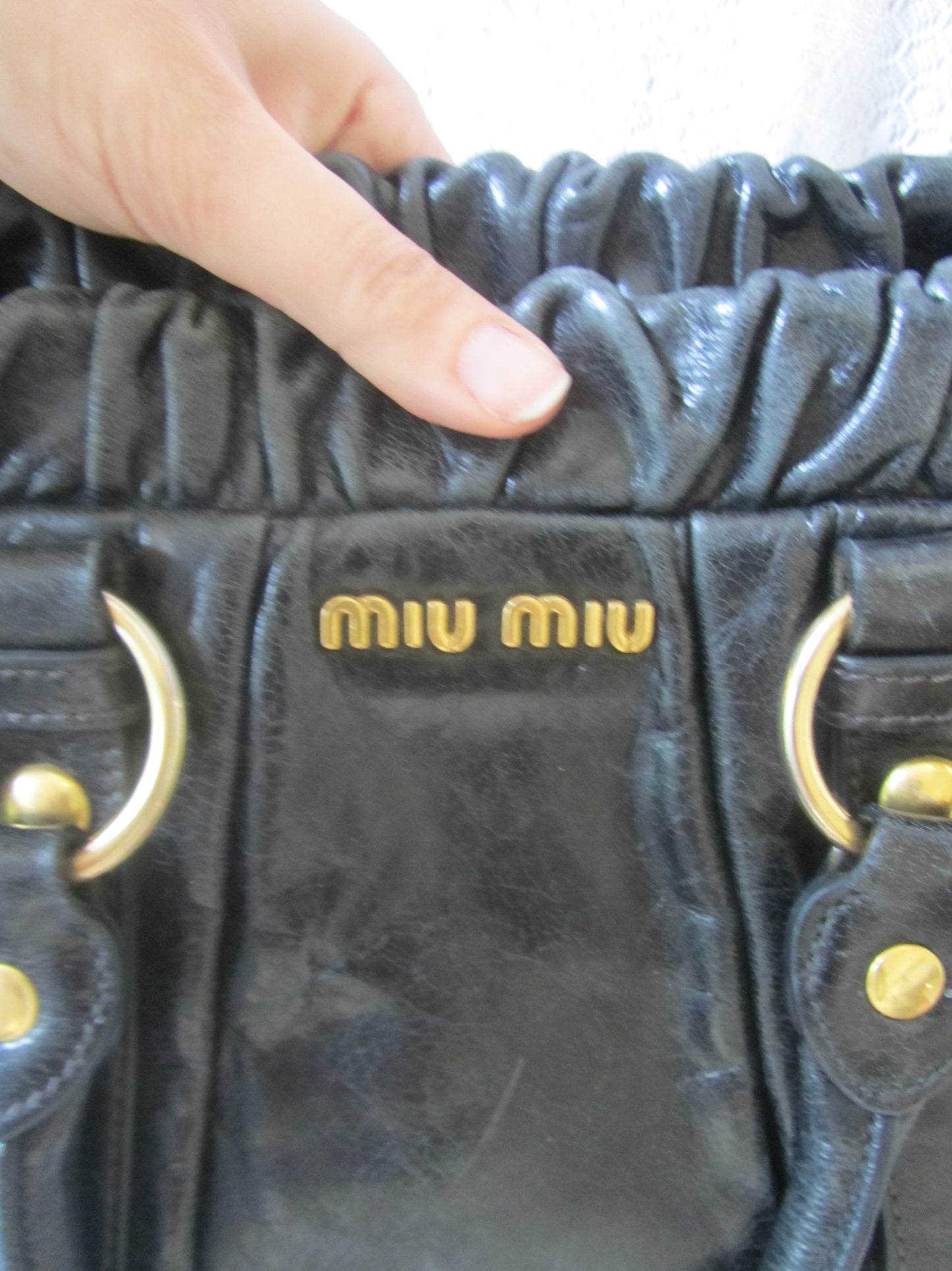 Black textured handbag with gold accents and 'Miu Miu' logo held by a hand.