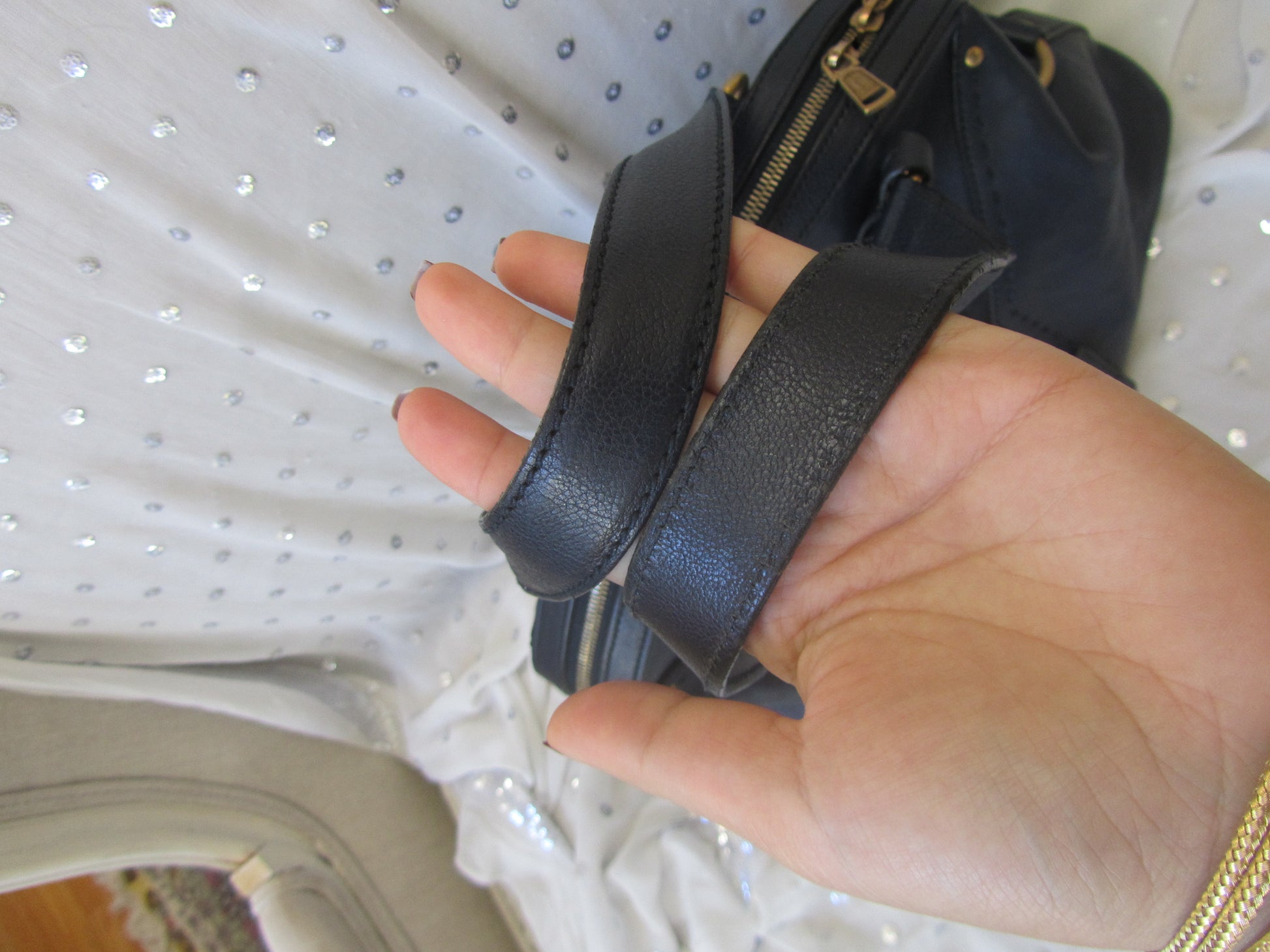 Hand holding a black leather strap with a gold zipper, blurred background