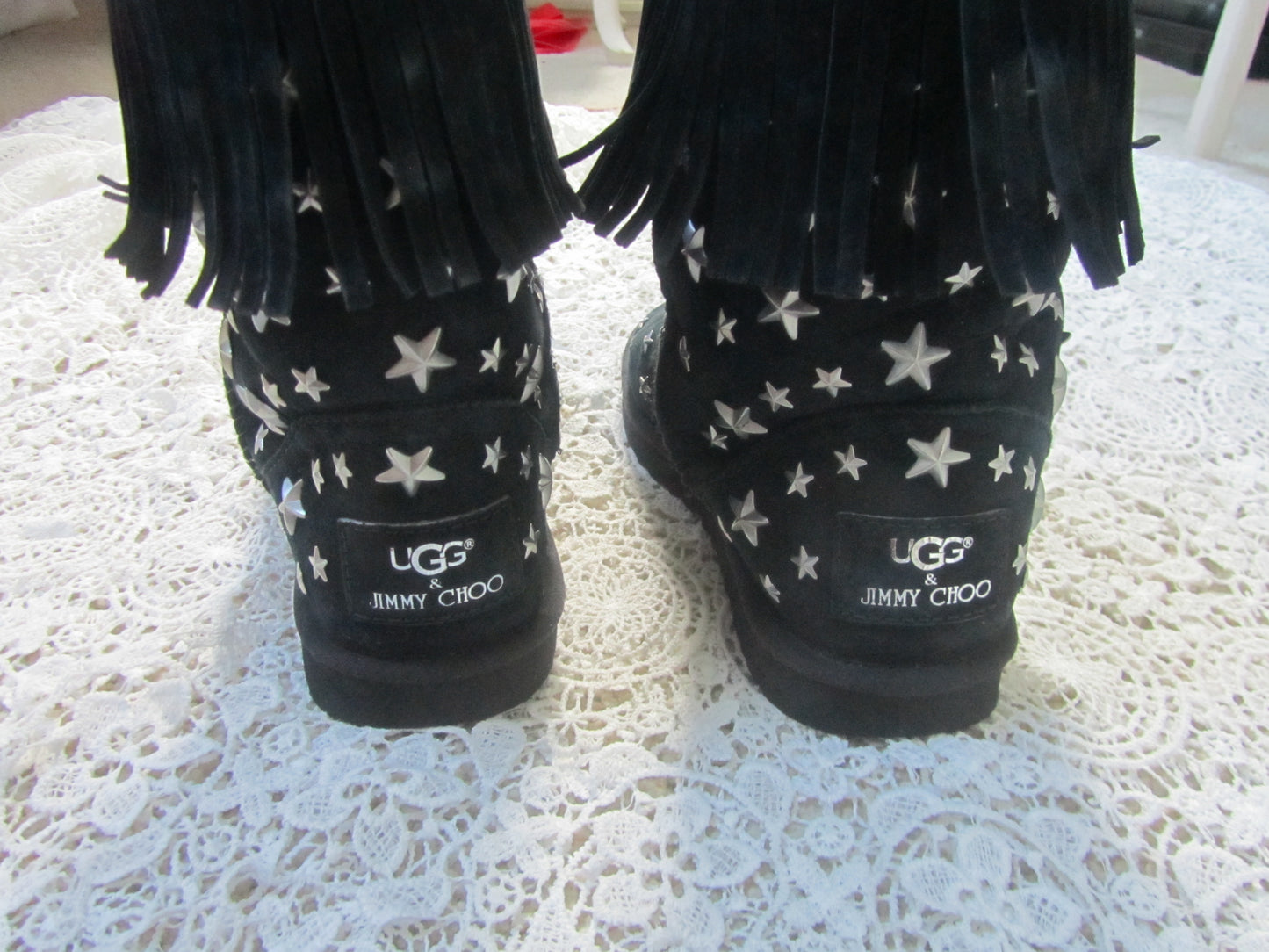 Black UGG boots with star pattern and 'JIMMY CHOO' branding on a textured white surface.