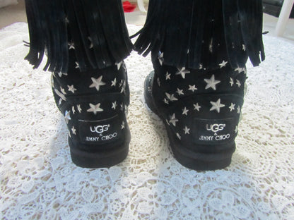 Black UGG boots with star pattern and 'JIMMY CHOO' branding on a textured white surface.