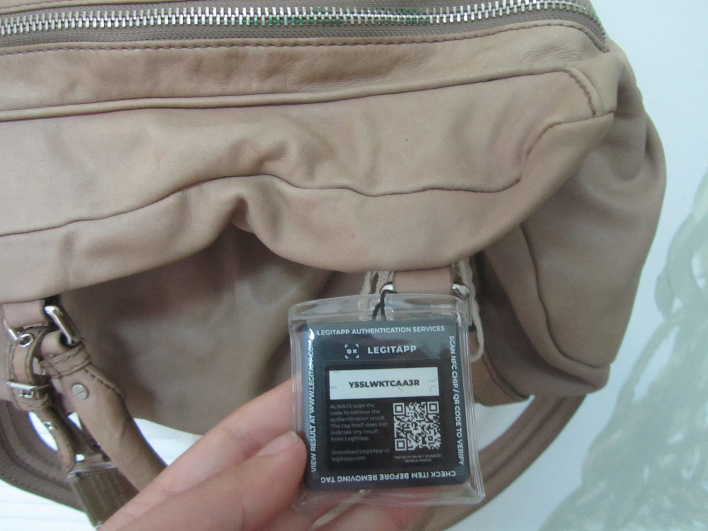 Beige handbag with a security tag featuring a QR code held by a hand against a light background