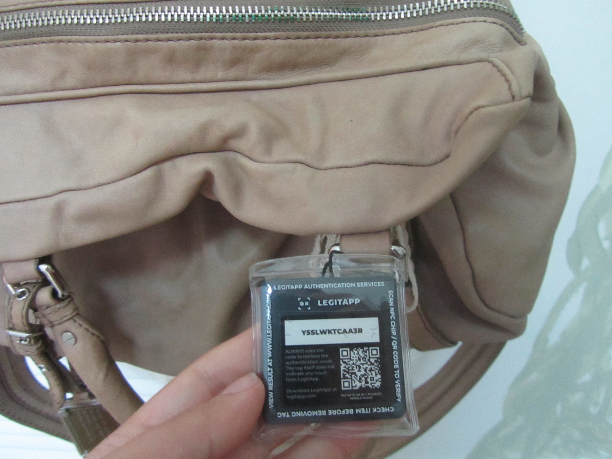 Beige handbag with a security tag featuring a QR code held by a hand against a light background