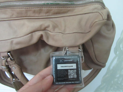 Beige handbag with a security tag featuring a QR code held by a hand against a light background