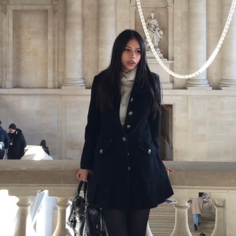 Woman in a black coat standing in front of a classical building with columns.