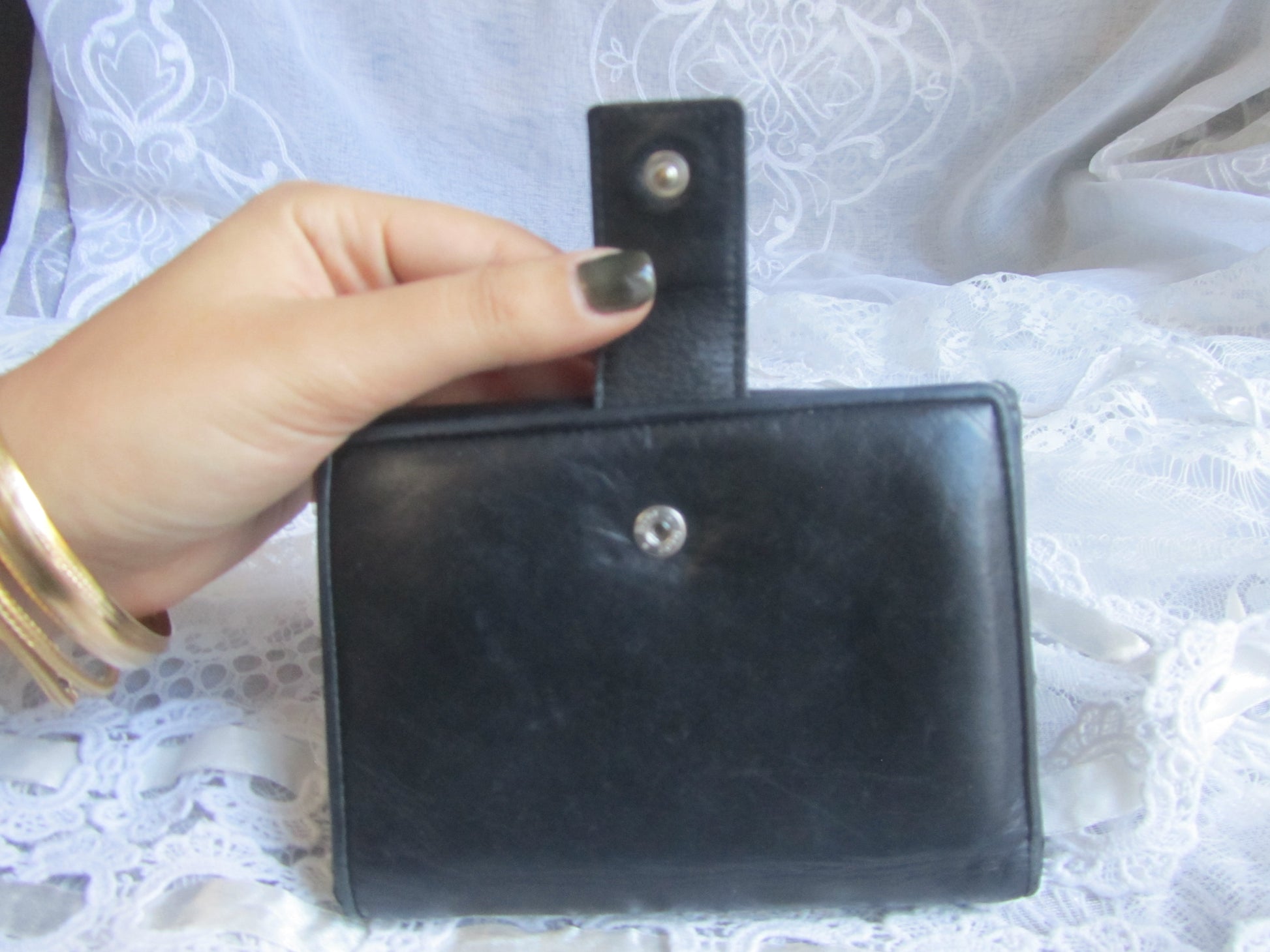 Black leather wallet held by a hand on a white lace background