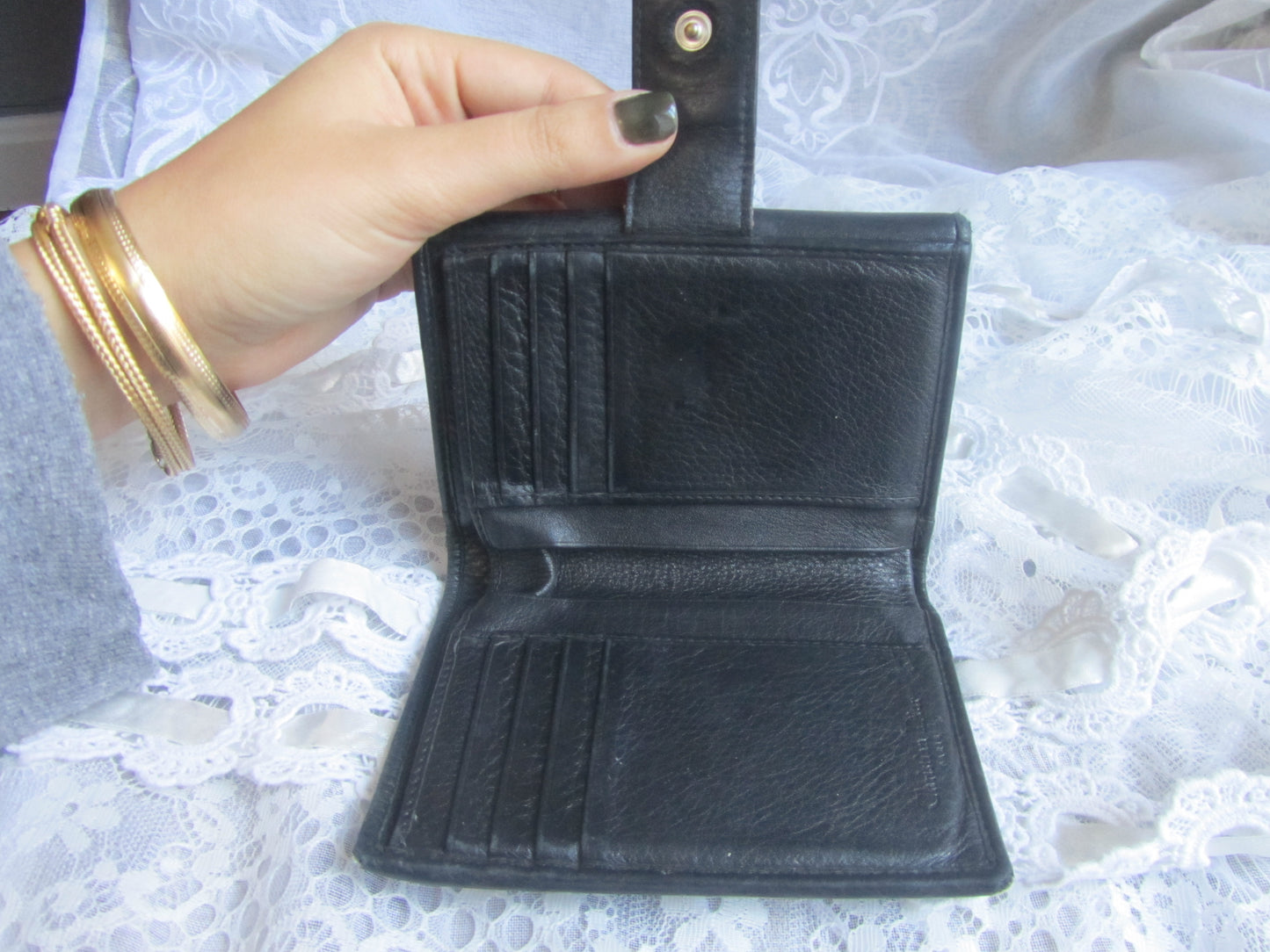Black leather wallet held open by a hand on a textured white background