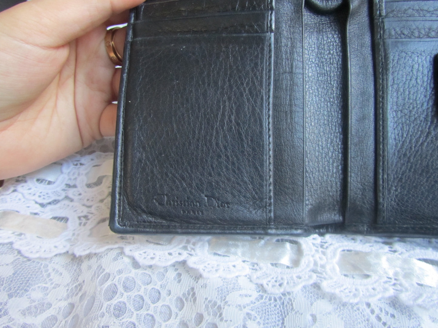 Black leather wallet held by a hand on a lace surface