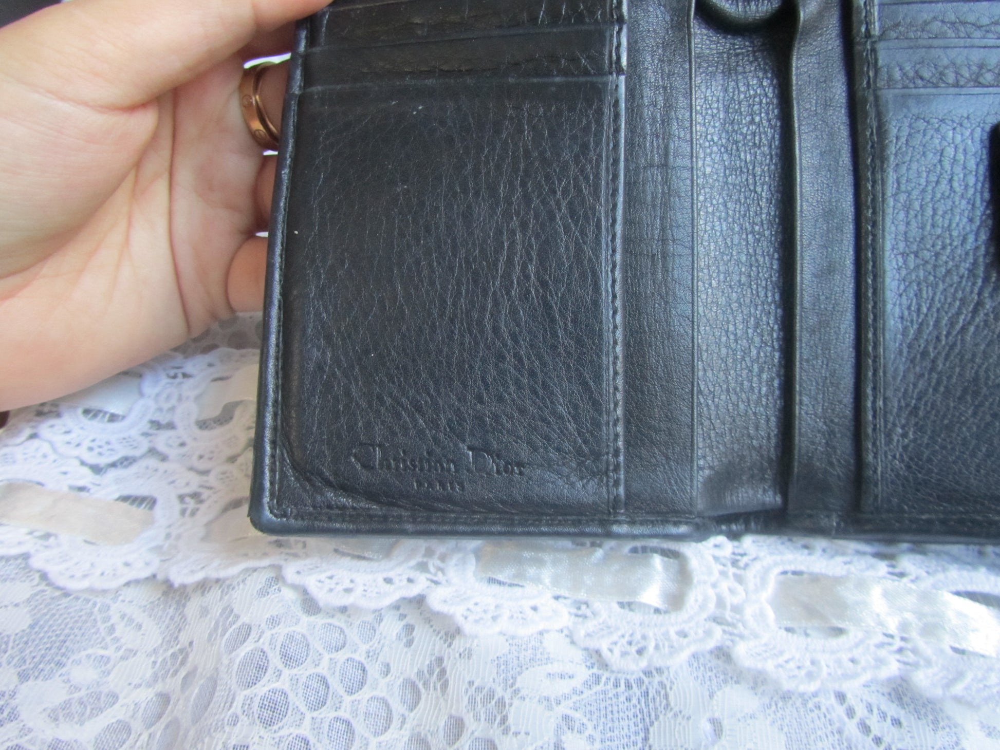 Black leather wallet held by a hand on a lace surface