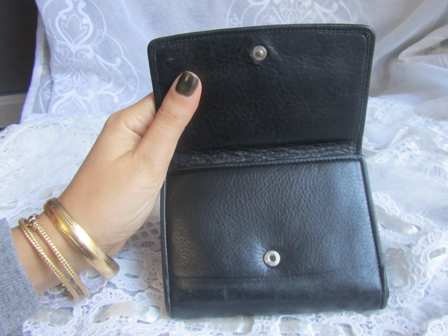Hand holding a black leather wallet on a white lace background