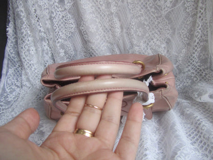 Pink handbag held by a hand with visible rings against a lace curtain background