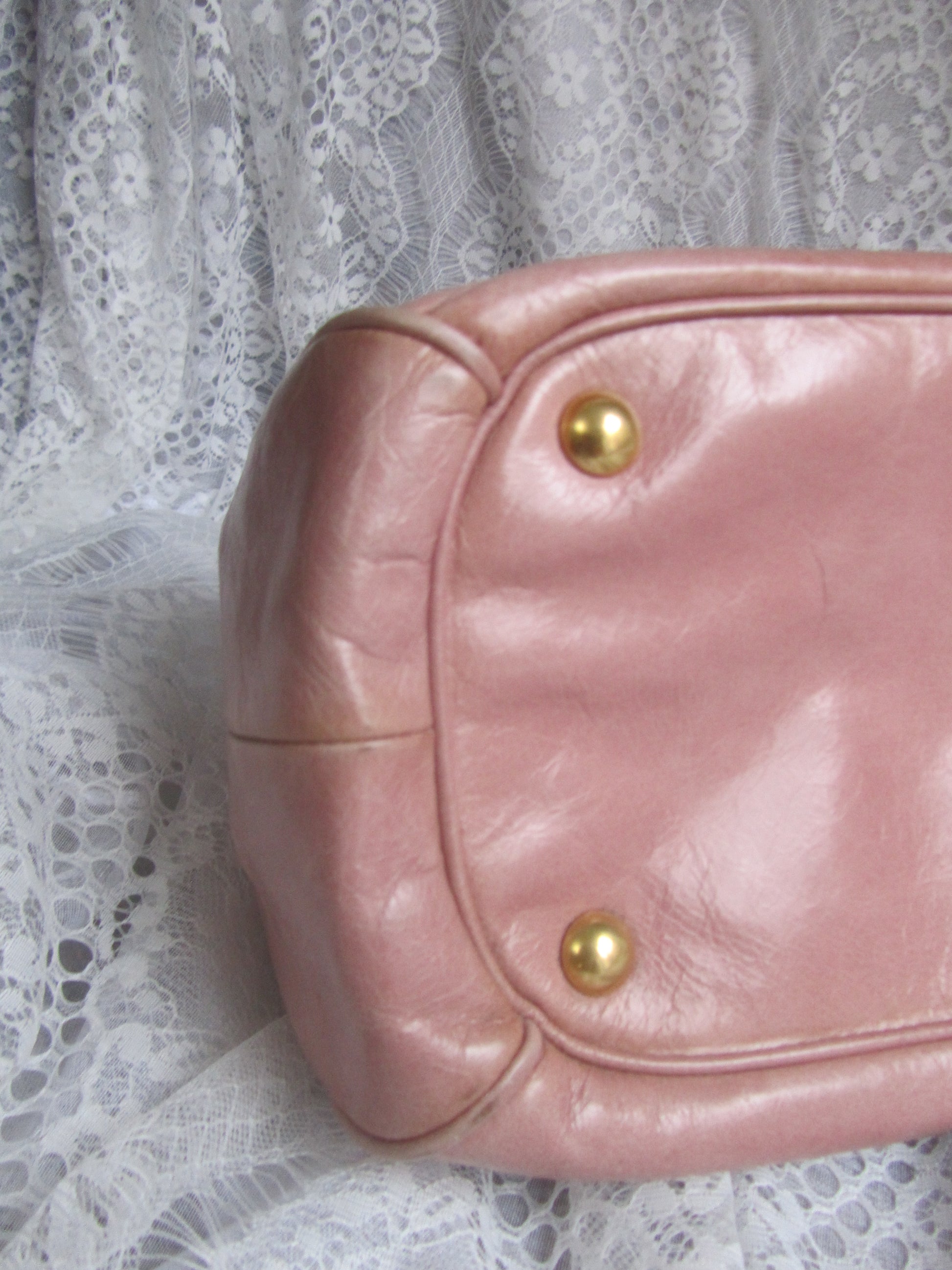 Pink leather handbag with gold studs on a lace background