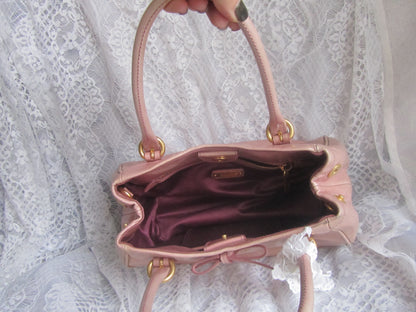 Pink handbag held by a hand against a lace background