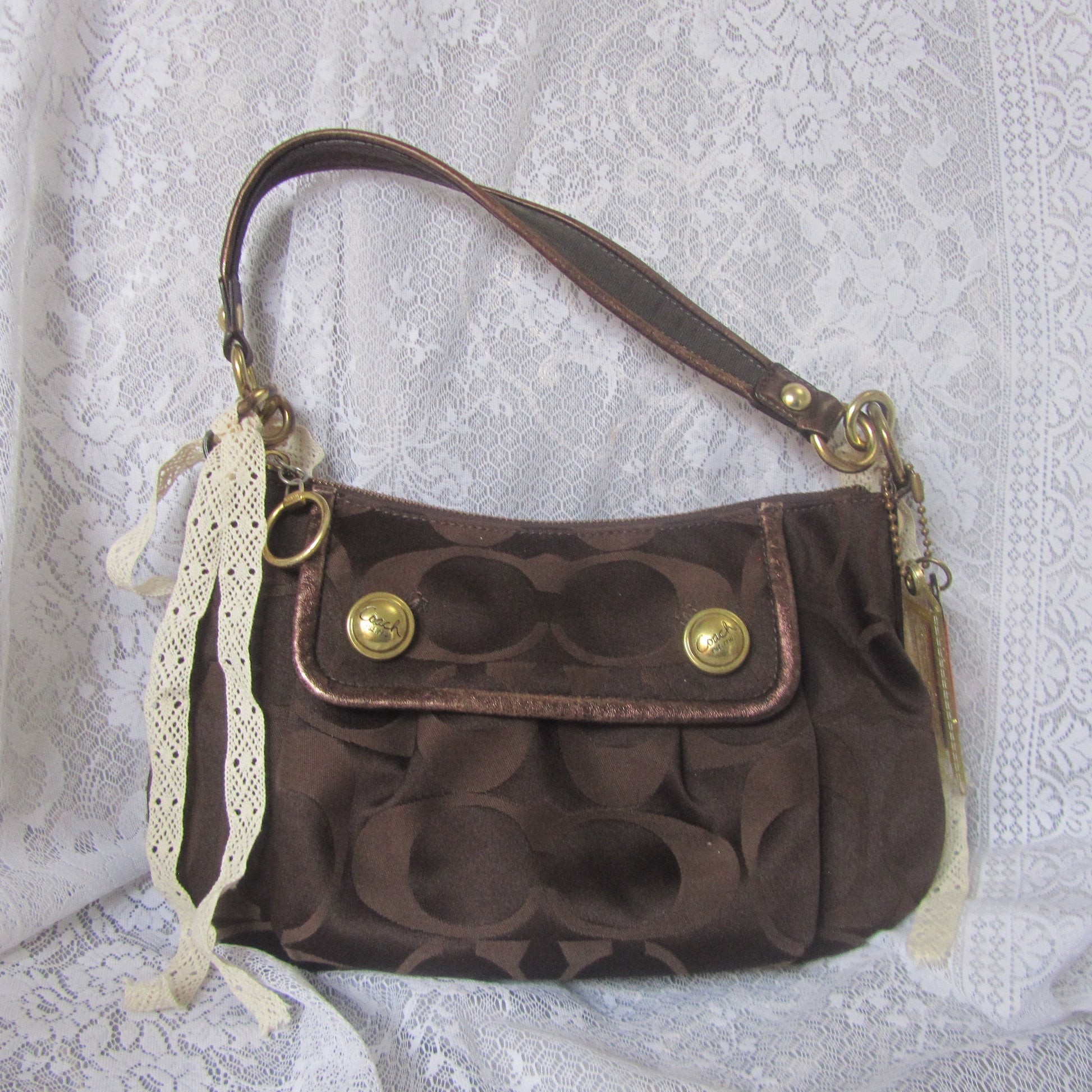 Brown textured handbag with gold accents on a white lace background