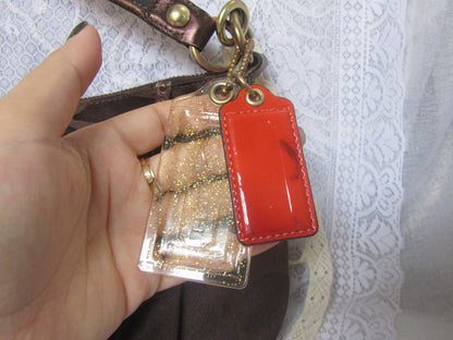 Hand holding a keychain with a red tag and gold chain against a white lace background