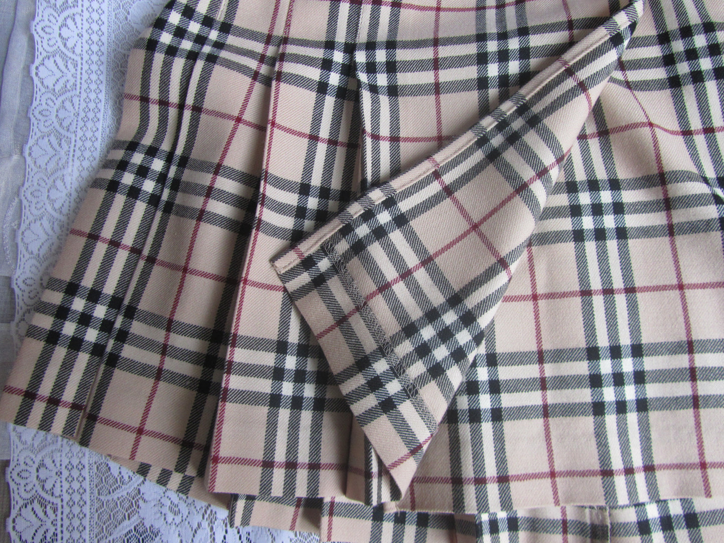 Plaid fabric with a beige, black, and red pattern on a textured surface.