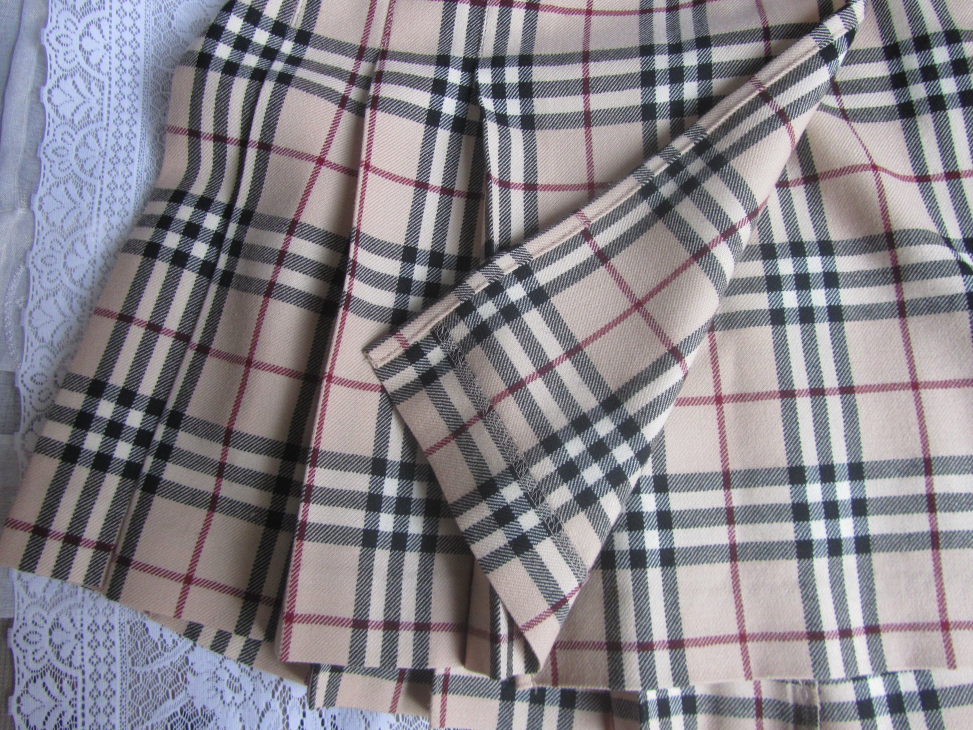 Plaid fabric with a beige, black, and red pattern on a textured surface.
