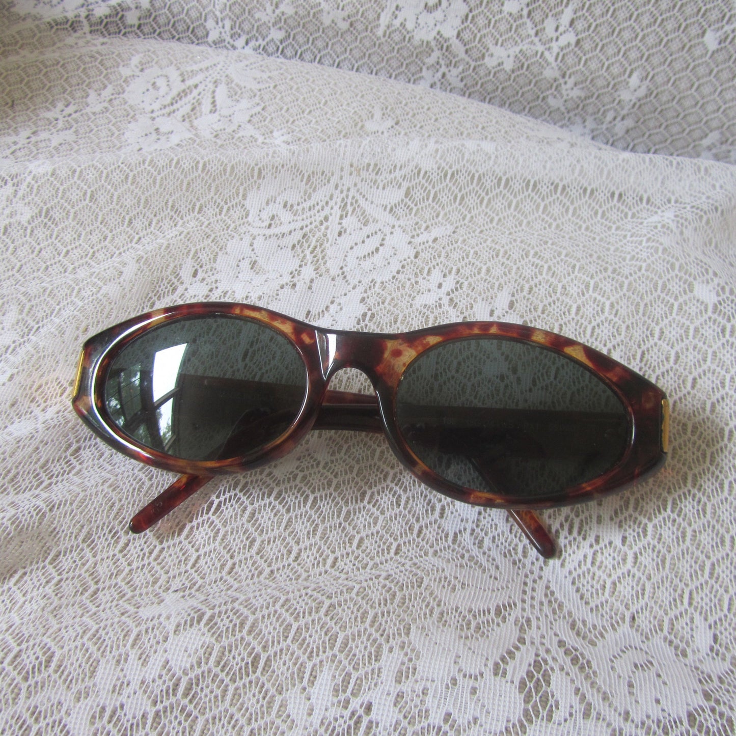 Sunglasses with tortoiseshell frame and dark lenses on a lace fabric background