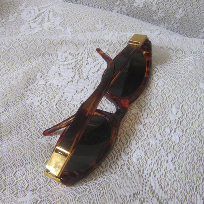 Sunglasses with tortoiseshell frame and gold accents on a lace surface